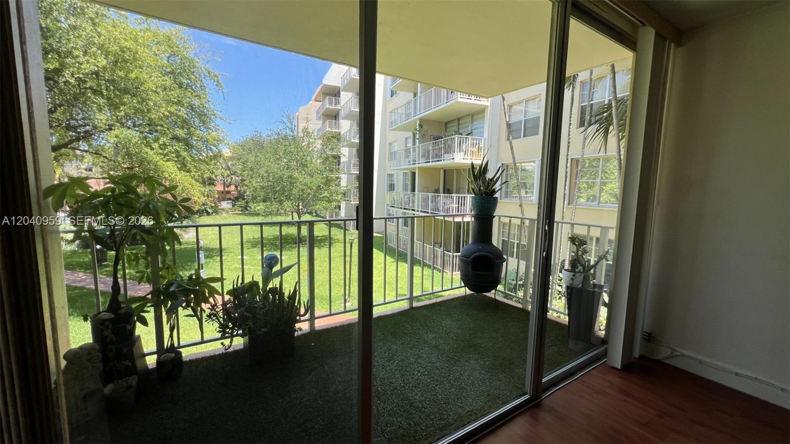 A balcony with artificial turf flooring overlooks a grassy courtyard and adjacent apartment buildings — 13120 SW 92nd Ave # 209, Miami FL 33176, MIAMI, FL