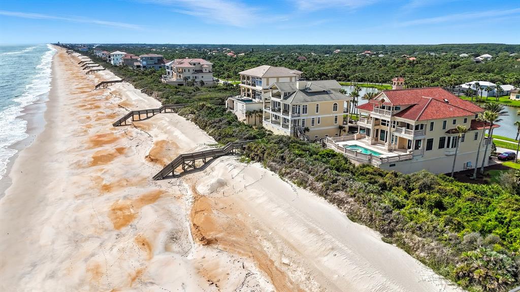 An aerial view shows luxury beachfront homes with private beach access stairs along the coast — 3715 N OCEAN SHORE BOULEVARD, PALM COAST, FL