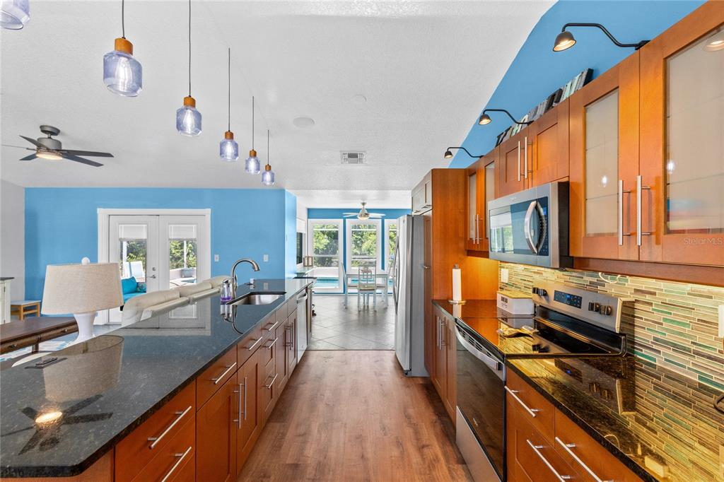 A kitchen with wood cabinets, granite countertops, and a tiled backsplash opens to a living area — 3951 SANTA BARBARA ROAD, KISSIMMEE, FL