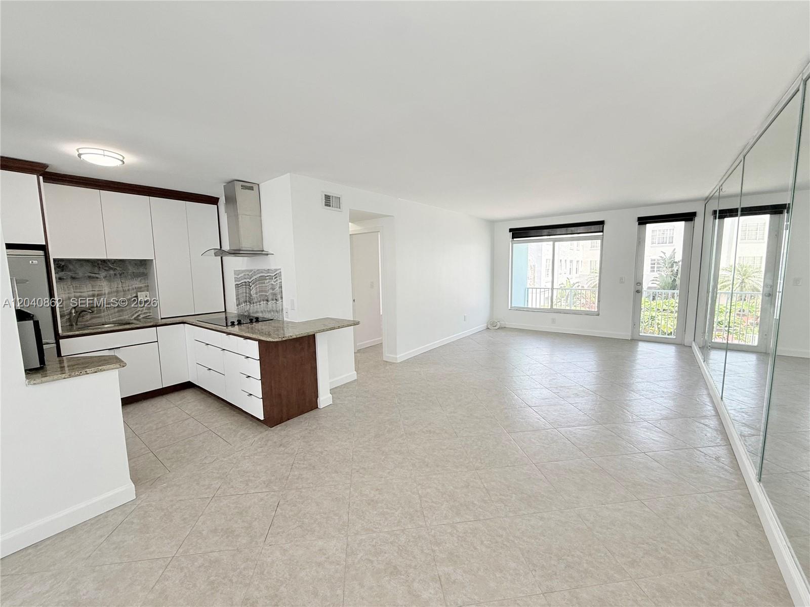 An open-concept kitchen and living area features white cabinetry, tiled floors, and a balcony door — 1150 Euclid Ave # 210, Miami Beach FL 33139, MIAMI BEACH, FL
