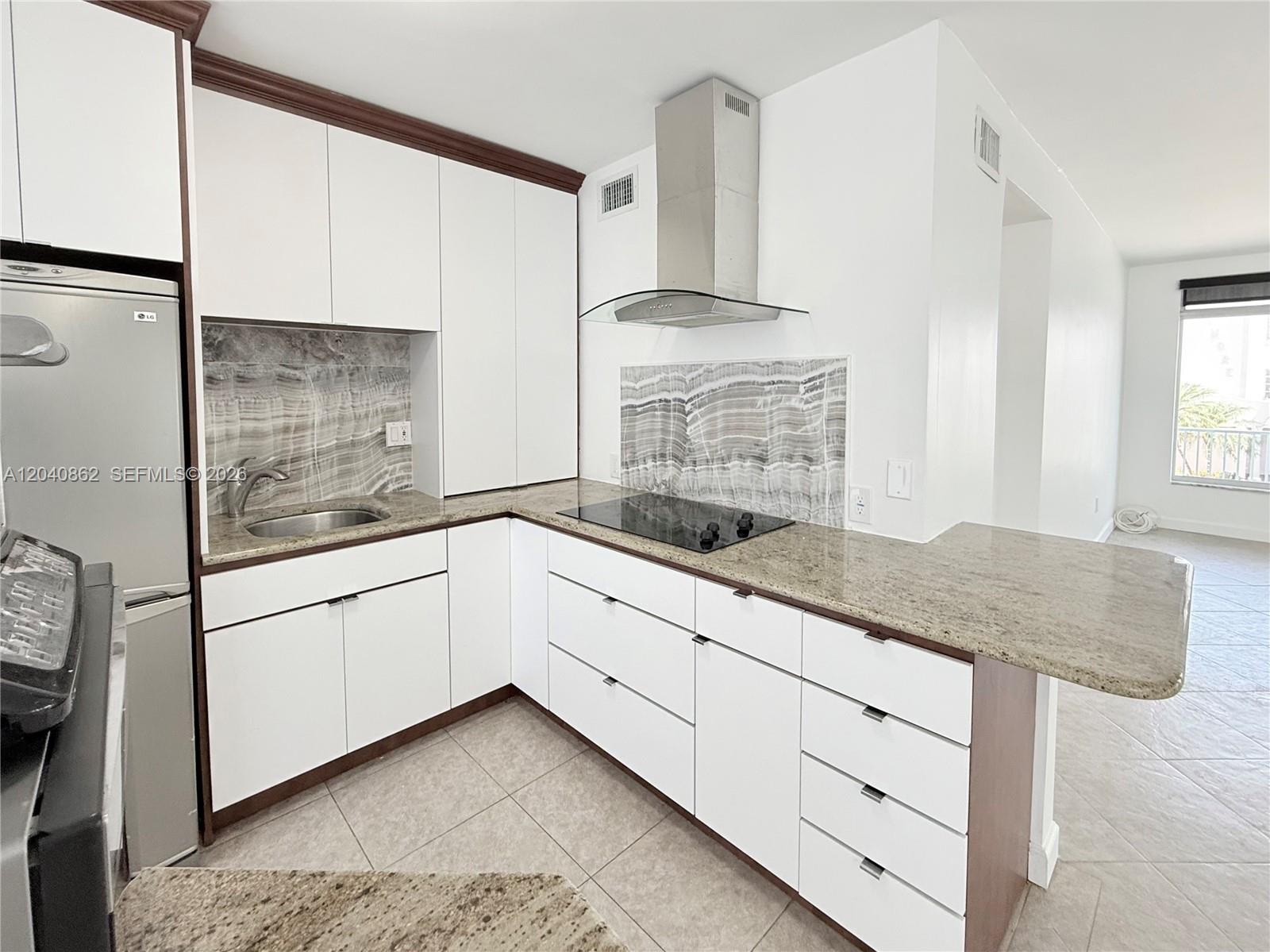 A kitchen features white cabinets, granite countertops, a stainless steel range hood, and stone backsplashes — 1150 Euclid Ave # 210, Miami Beach FL 33139, MIAMI BEACH, FL
