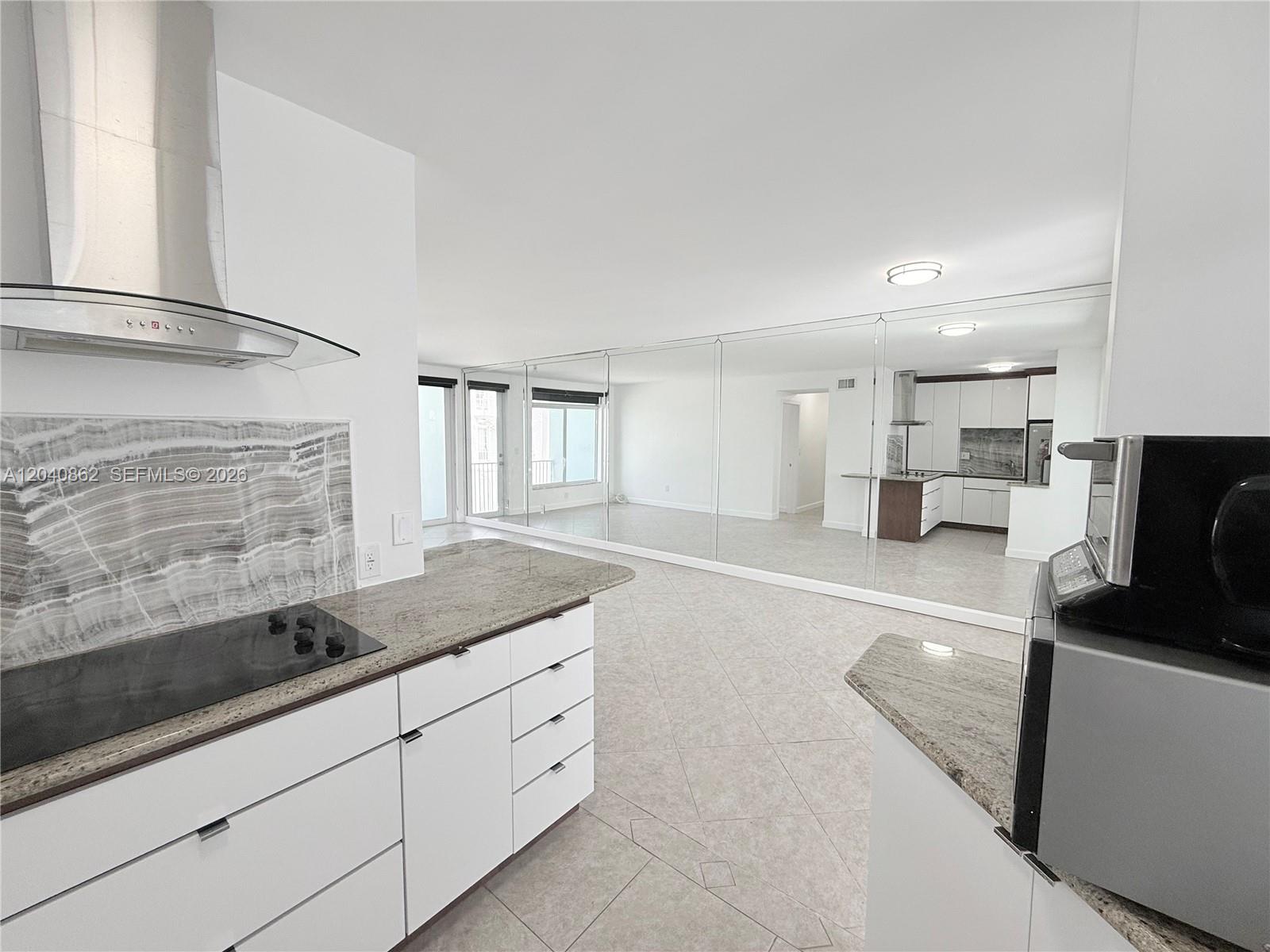 A kitchen with white cabinets and granite countertops overlooks a living area with mirrored walls — 1150 Euclid Ave # 210, Miami Beach FL 33139, MIAMI BEACH, FL