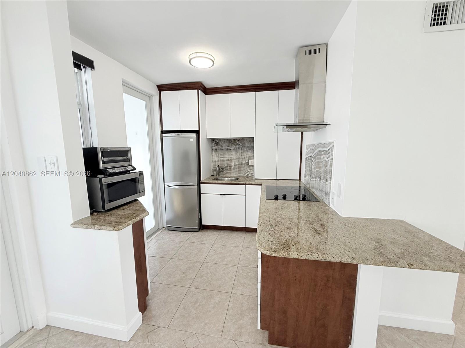 A kitchen features white cabinets, granite countertops, stainless steel appliances, and tile flooring — 1150 Euclid Ave # 210, Miami Beach FL 33139, MIAMI BEACH, FL