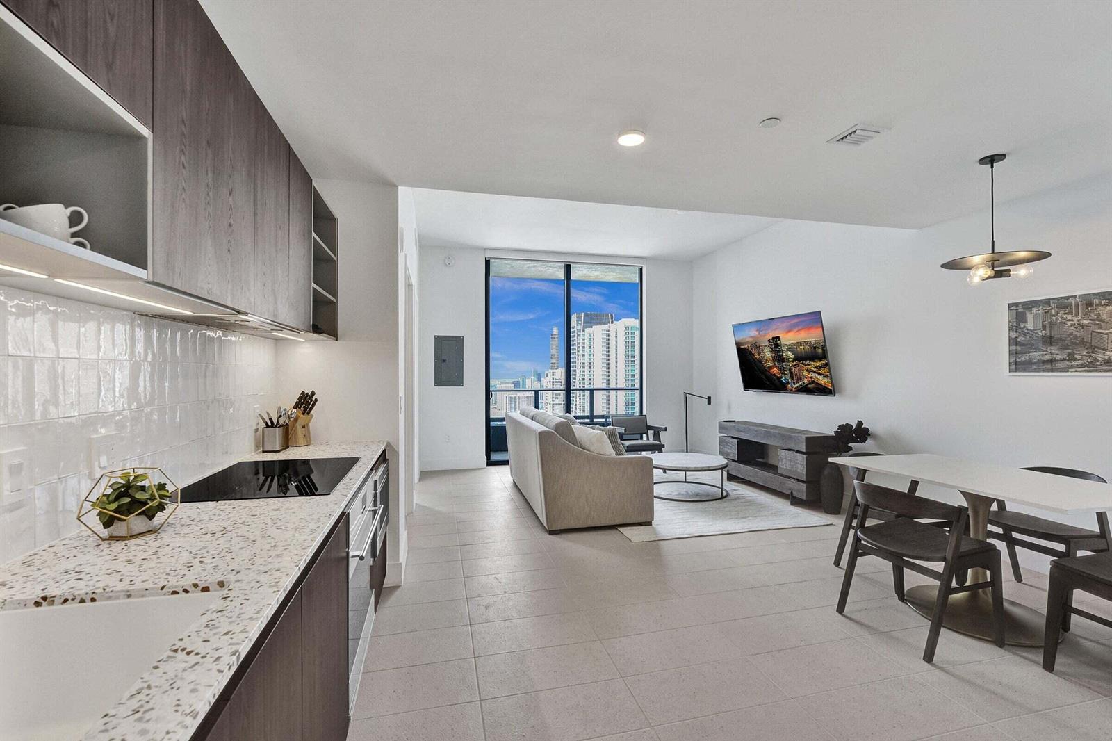 A modern open-concept kitchen and living area with floor-to-ceiling windows overlooking a city skyline — 159 NE 6th Street # 4813, Miami FL 33132, MIAMI, FL