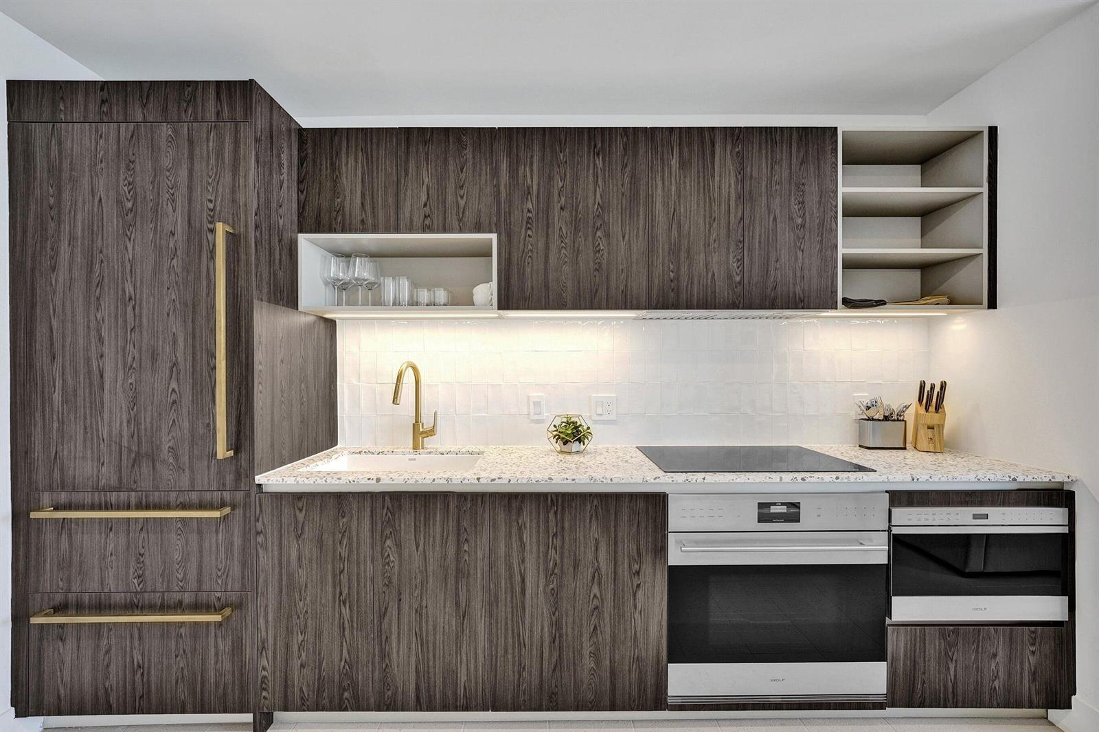 A modern kitchen features dark wood cabinetry, gold hardware, white tile backsplash, and speckled countertops — 159 NE 6th Street # 4813, Miami FL 33132, MIAMI, FL