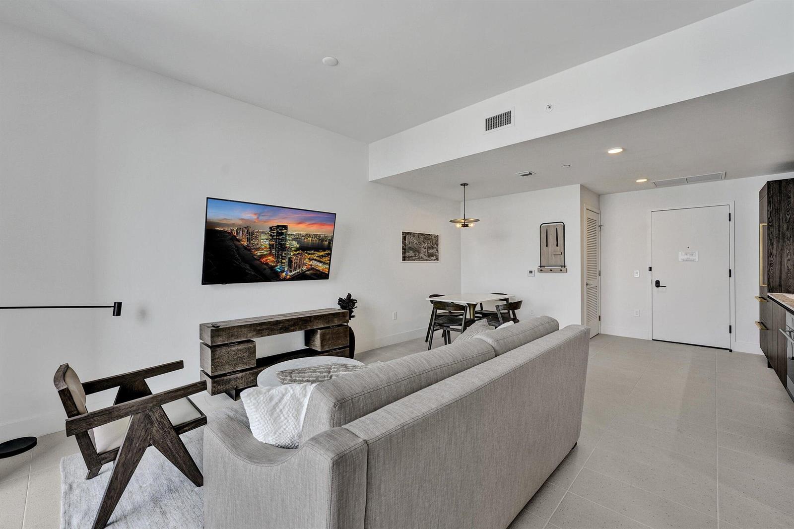 A modern living room features a grey sofa, a wooden media console, and a dining area — 159 NE 6th Street # 4813, Miami FL 33132, MIAMI, FL