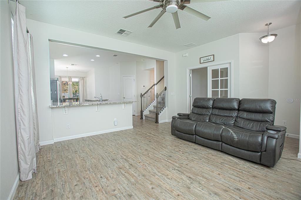 A living room with wood-look flooring, a dark leather sofa, and an open kitchen view — 2427 LINER AVENUE, APOPKA, FL