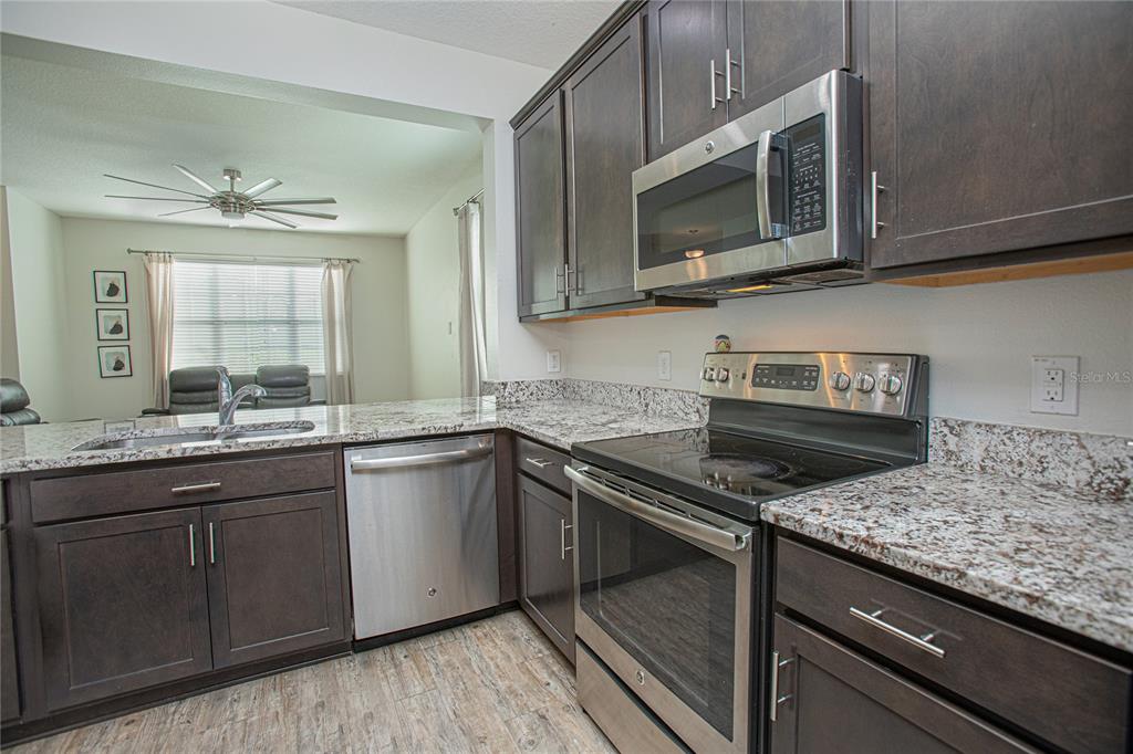 A kitchen features dark wood cabinets, stainless steel appliances, and granite countertops — 2427 LINER AVENUE, APOPKA, FL