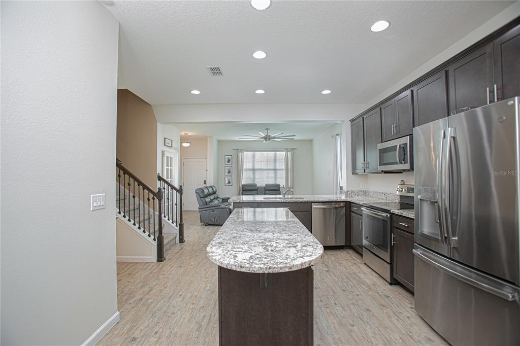 A kitchen with dark cabinets, granite countertops, and stainless steel appliances overlooks a living area — 2427 LINER AVENUE, APOPKA, FL