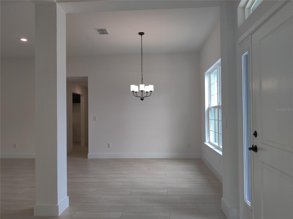 A dining area features light-colored tile flooring, a central chandelier, and a white front door — 12275 SCARLET IBIS AVENUE, WEEKI WACHEE, FL