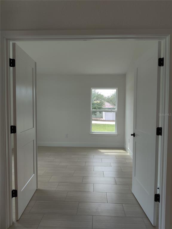 A view through double doors into a room with light-colored tile flooring and a window — 12275 SCARLET IBIS AVENUE, WEEKI WACHEE, FL