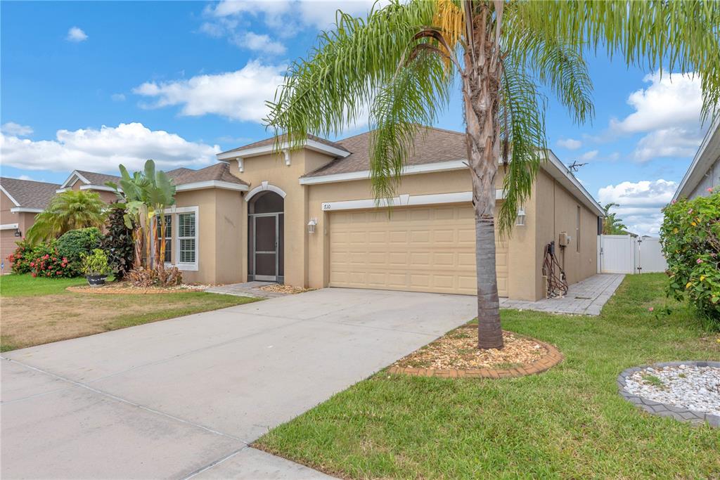 A single-story tan house with a two-car garage and a palm tree in front — 710 PARKER DEN DRIVE, RUSKIN, FL