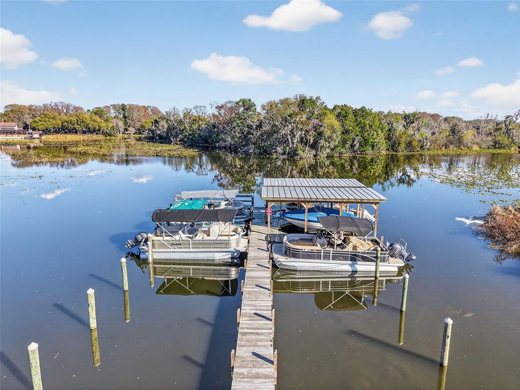 A wooden dock extends into a lake with two pontoon boats moored alongside it — 913 BELLE OAK DRIVE UNIT 0, LEESBURG, FL