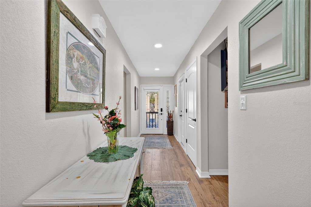 A hallway with wood-look flooring, a white console table, and a glass-paneled front door — 913 BELLE OAK DRIVE UNIT 0, LEESBURG, FL