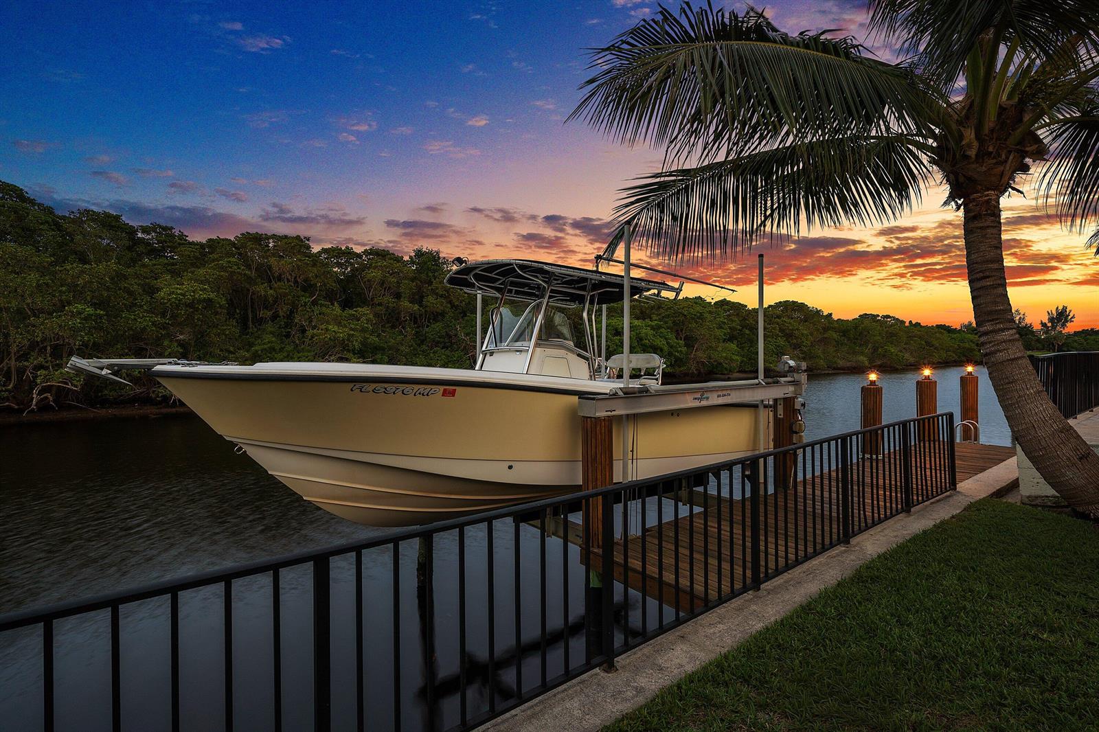 A cream-colored center console boat sits on a lift at a dock during sunset — 763 Camino Lakes Circle, Boca Raton FL 33486, BOCA RATON, FL