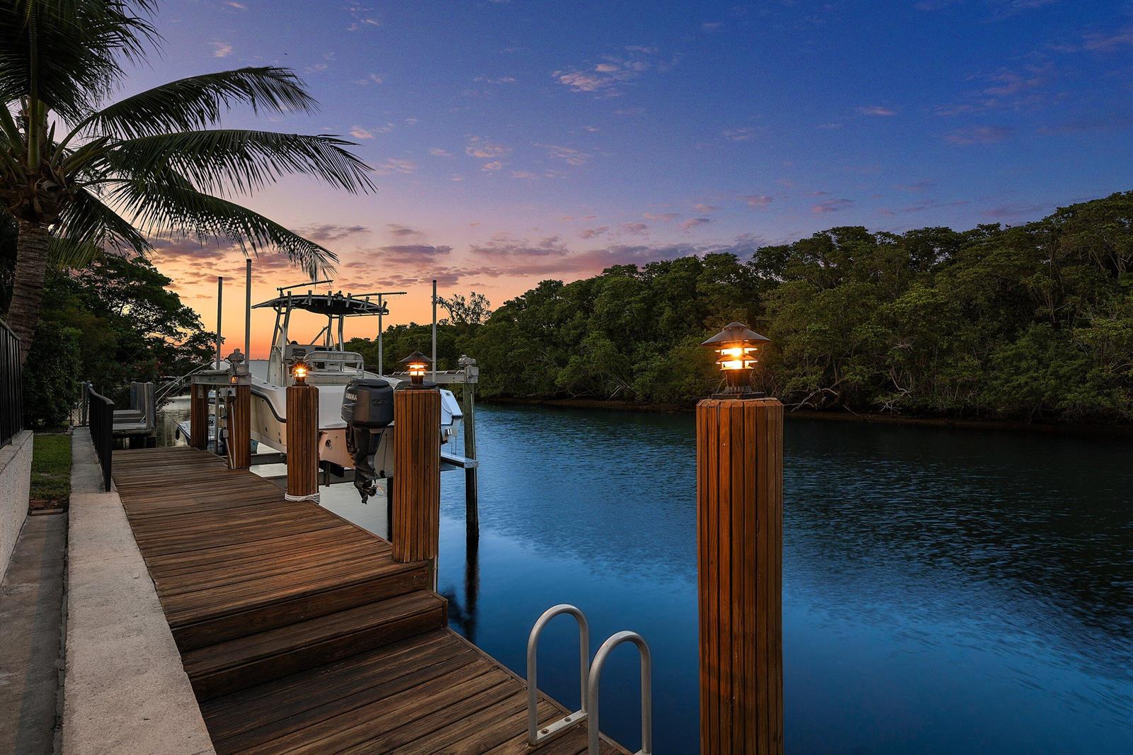 A wooden dock with a boat lift and illuminated posts overlooks a canal at sunset — 763 Camino Lakes Circle, Boca Raton FL 33486, BOCA RATON, FL