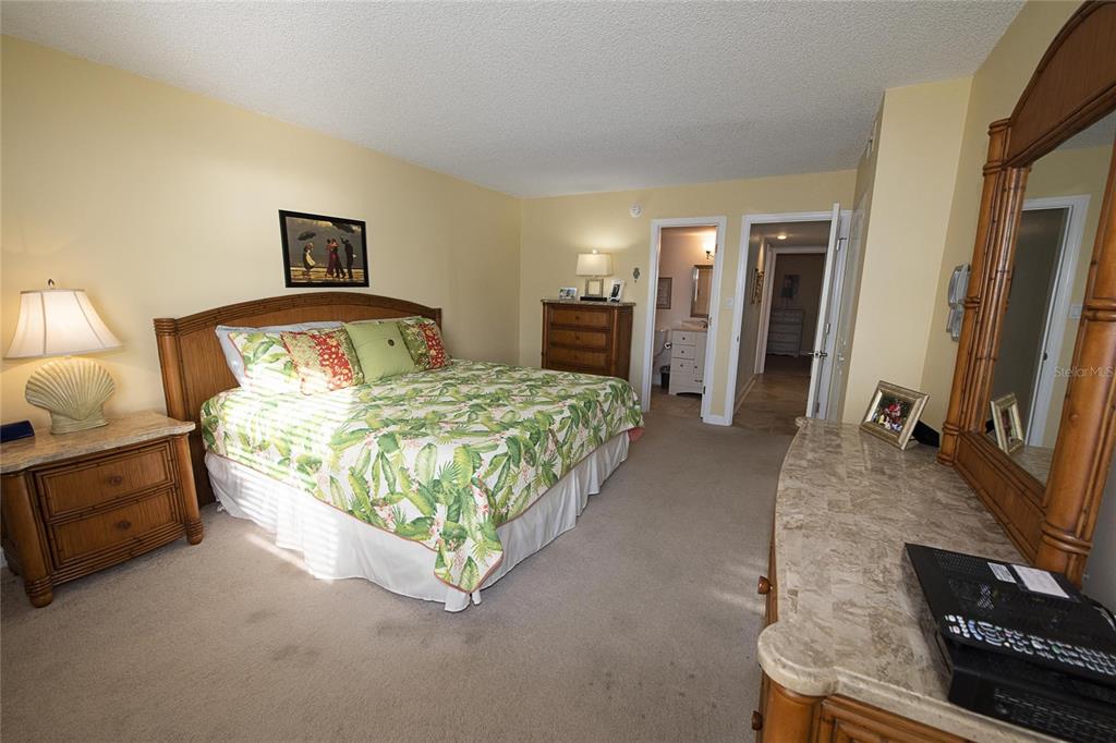 A bedroom features a tropical-themed bed, a wooden dresser, and an attached bathroom — 1571 S ATLANTIC AVENUE UNIT 306, NEW SMYRNA BEACH, FL