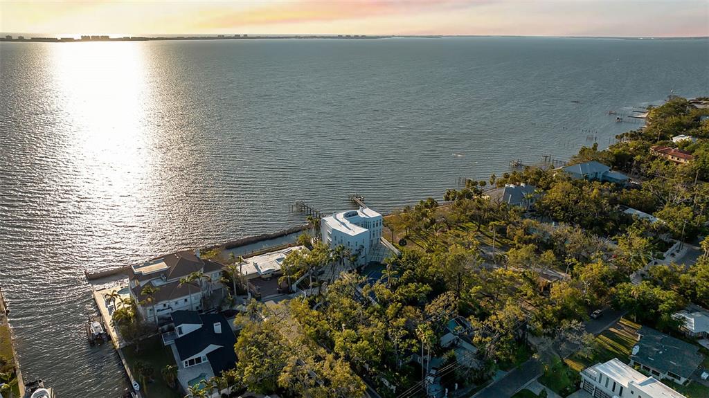 An aerial view shows a white waterfront house surrounded by trees along a large bay — 2043 ALAMEDA AVENUE, SARASOTA, FL