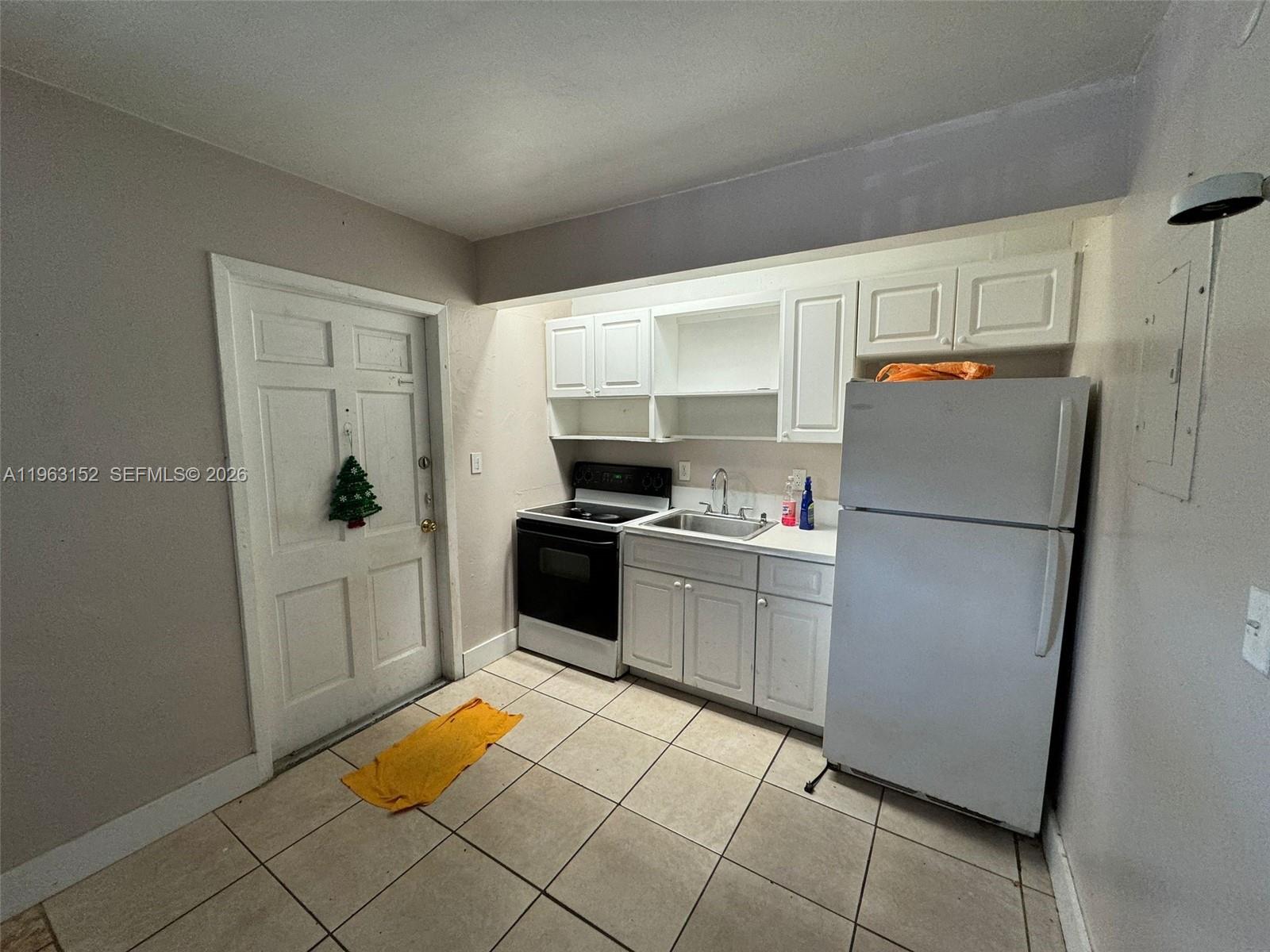 A small kitchen features white cabinets, a black stove, a refrigerator, and tiled flooring — 7841 Dunham Blvd # 1, Miami FL 33138, MIAMI, FL