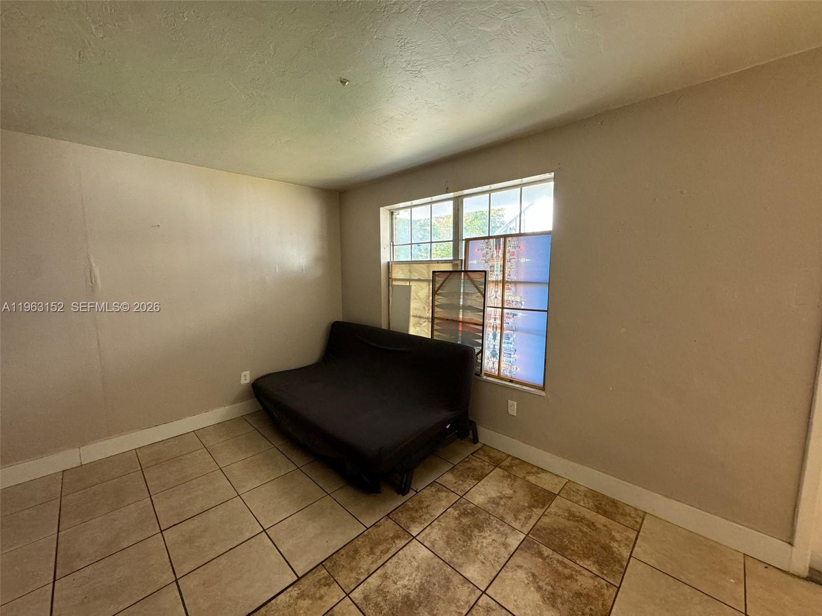 A room with beige walls, tiled flooring, and a black futon placed under a window — 7841 Dunham Blvd # 1, Miami FL 33138, MIAMI, FL