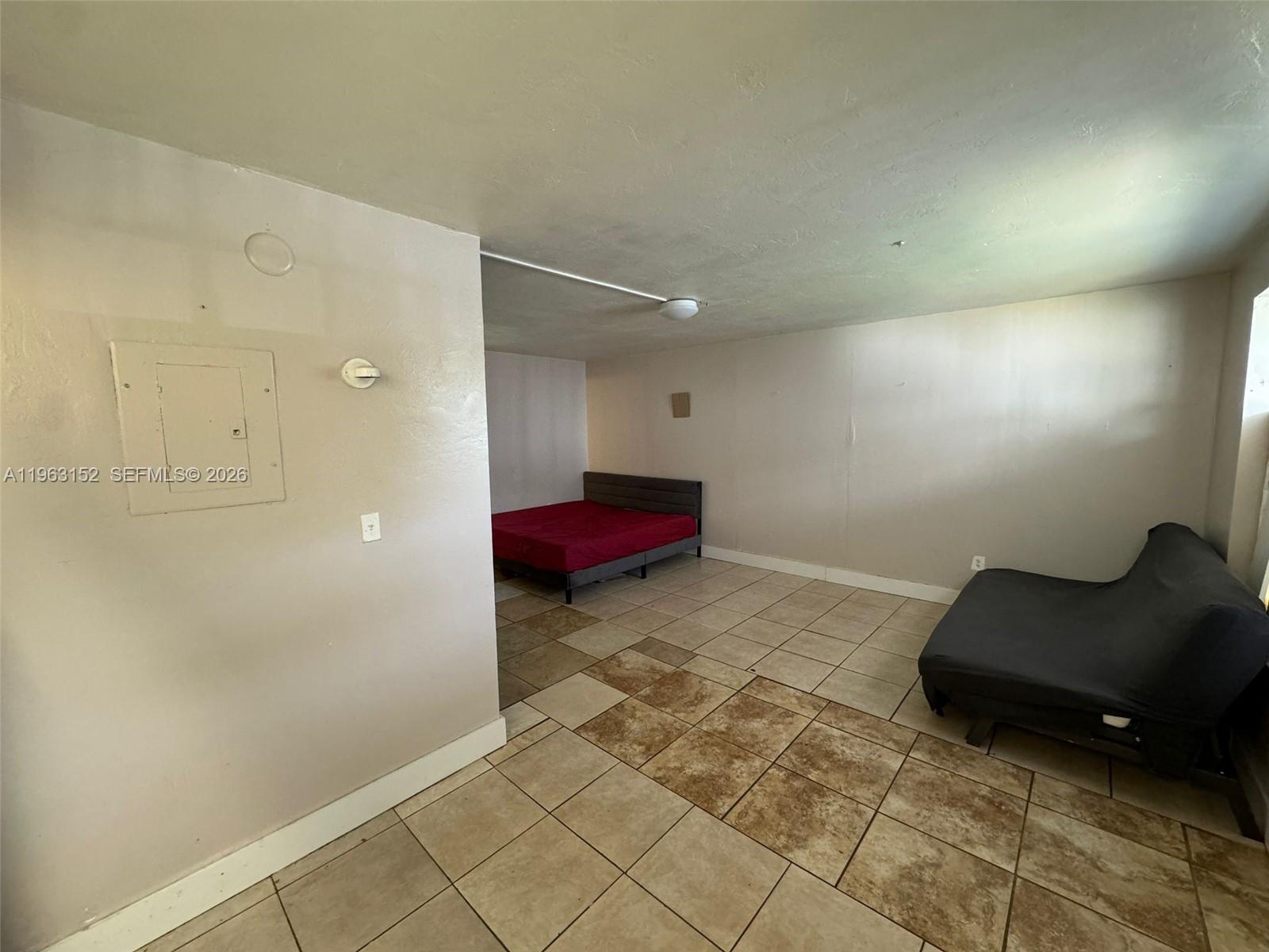 A room with tile flooring, a bed in the back, and a futon in the foreground — 7841 Dunham Blvd # 1, Miami FL 33138, MIAMI, FL