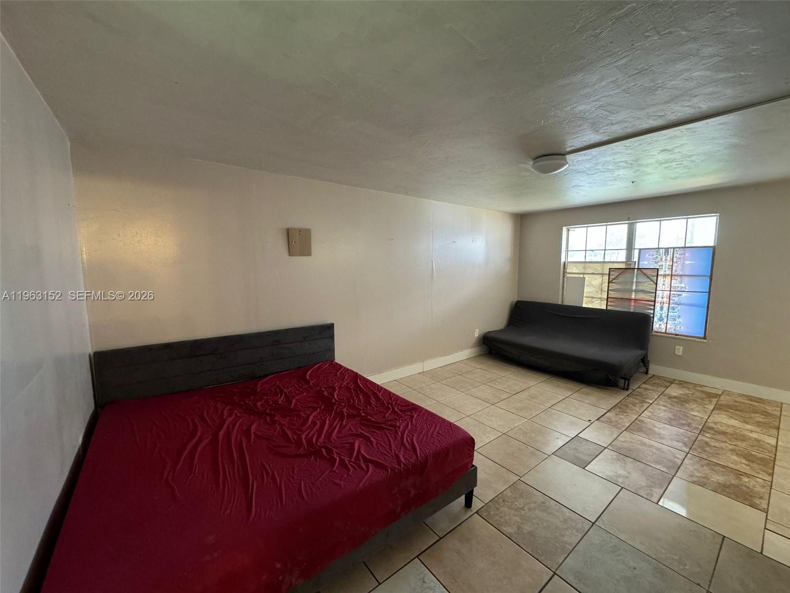 A bedroom with tiled floors, a bed with a red sheet, and a dark futon — 7841 Dunham Blvd # 1, Miami FL 33138, MIAMI, FL