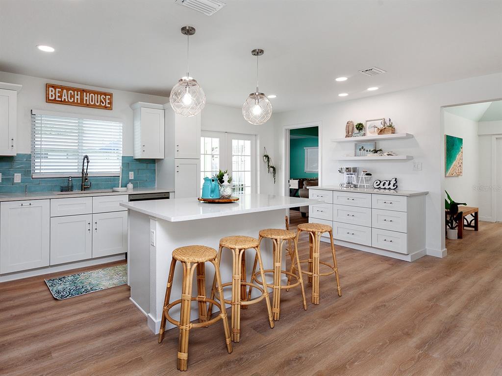 A bright kitchen features white cabinetry, a central island with rattan stools, and blue backsplash — 3049 WOOD STREET, SARASOTA, FL