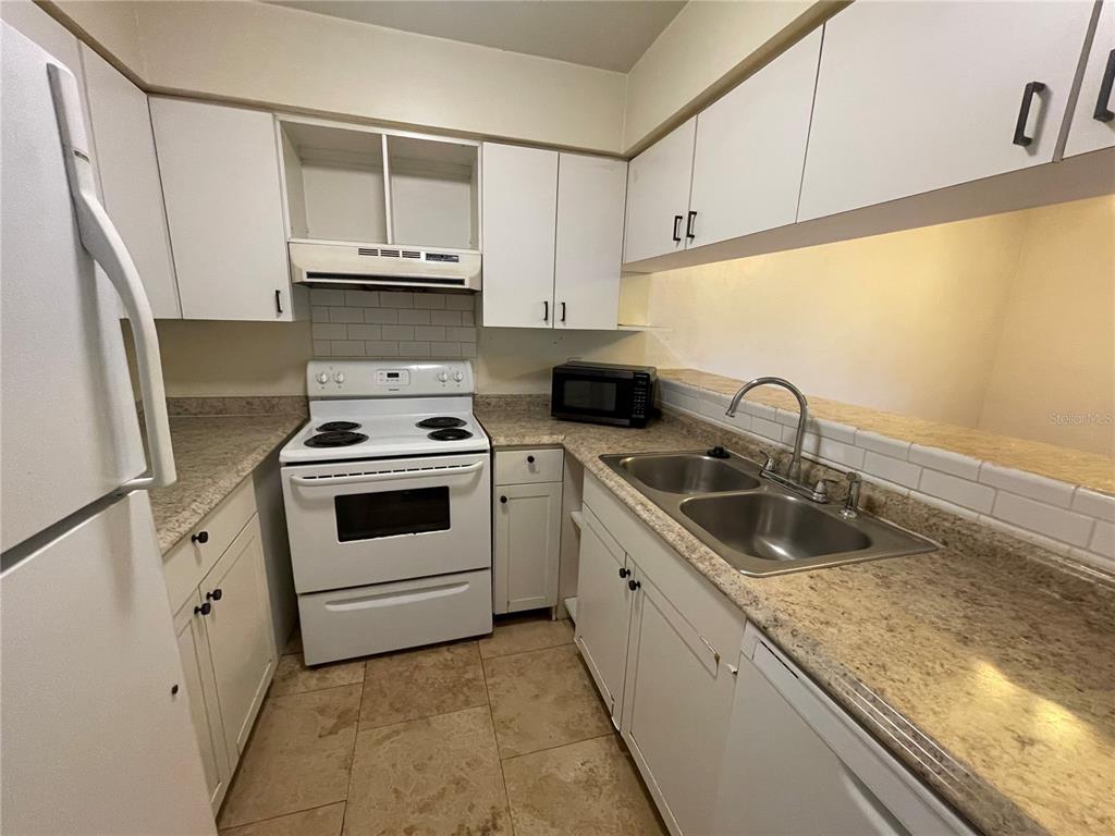A kitchen features white cabinets, a white stove, a double sink, and tan countertops — 2735 SW 35 PLACE UNIT 1607, GAINESVILLE, FL
