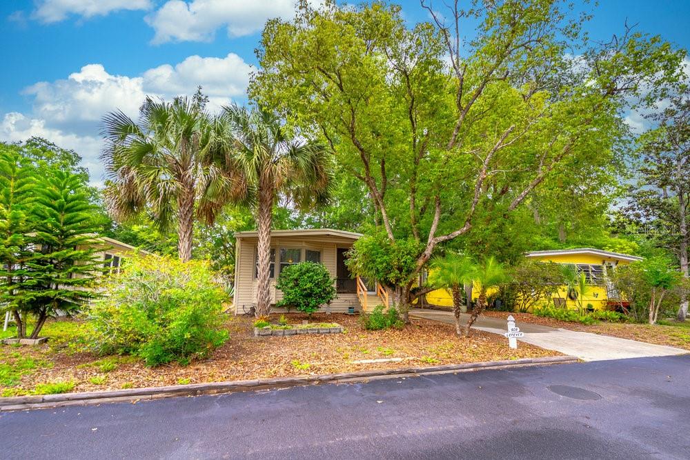 A tan mobile home with a driveway and mature trees sits behind a paved street — 508 W PLANTATION BOULEVARD, LAKE MARY, FL