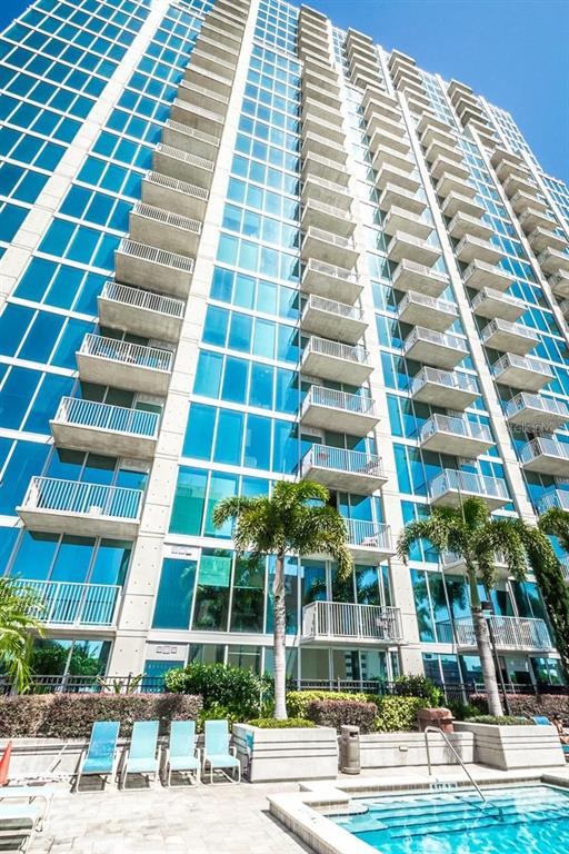 A tall, modern glass high-rise apartment building features numerous balconies overlooking a ground-level swimming pool — 777 N ASHLEY DRIVE UNIT 2403, TAMPA, FL