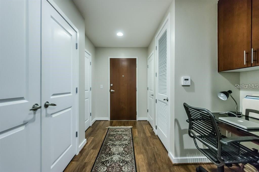 A hallway with wood-look flooring leads to a wooden front door near a small desk — 777 N ASHLEY DRIVE UNIT 2403, TAMPA, FL