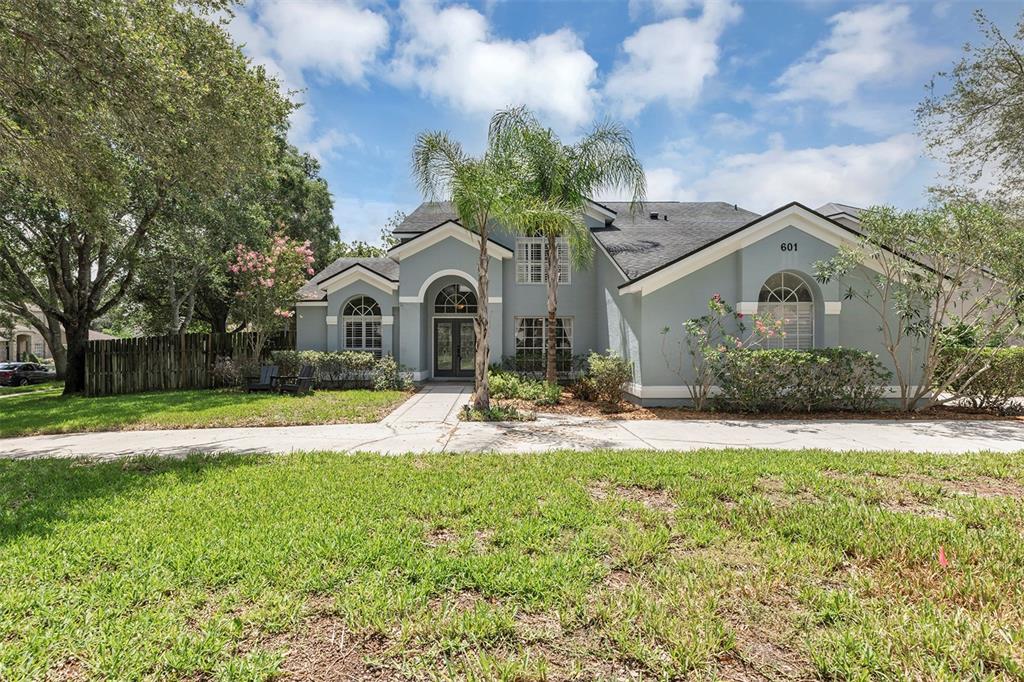 A light blue single-story house features a central arched entryway and a concrete driveway — 601 RED MAPLE COURT, OVIEDO, FL