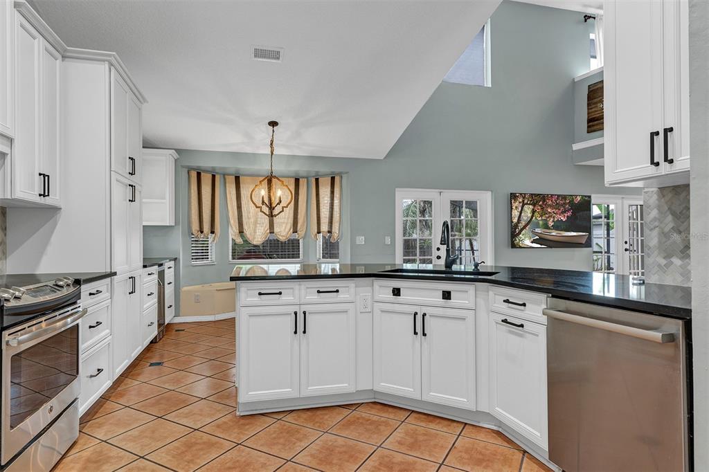 A kitchen with white cabinets, black countertops, and tile flooring features a breakfast nook area — 601 RED MAPLE COURT, OVIEDO, FL