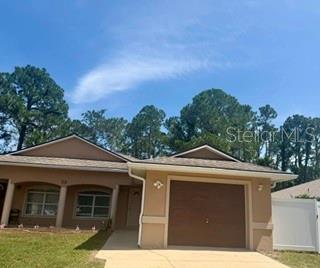 A single-story tan house with a one-car garage and a front porch under a blue sky — 22 PLATEAU LANE UNIT B, PALM COAST, FL