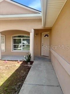 A concrete walkway leads to the front entrance of a tan stucco home — 22 PLATEAU LANE UNIT B, PALM COAST, FL