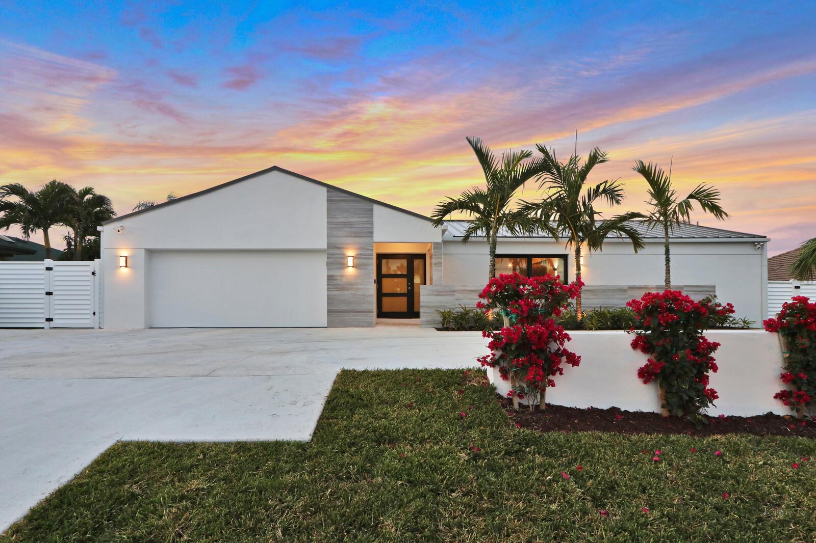 A modern single-story house with a white facade, wood-look accents, and palm trees at sunset — 441 S Lyra Circle, Juno Beach FL 33408, JUNO BEACH, FL