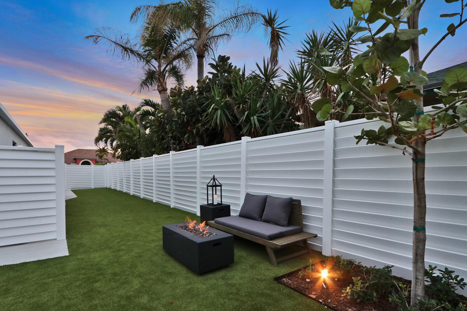 A backyard features a white vinyl fence, artificial turf, a fire pit, and a bench — 441 S Lyra Circle, Juno Beach FL 33408, JUNO BEACH, FL