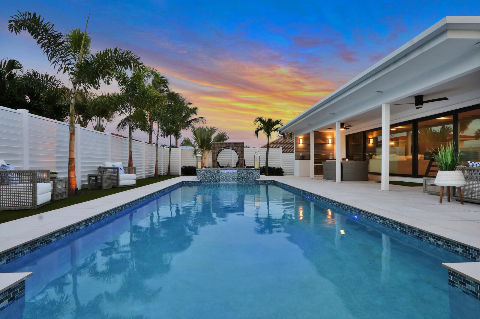 A swimming pool with a water feature sits in a backyard patio area at sunset — 441 S Lyra Circle, Juno Beach FL 33408, JUNO BEACH, FL