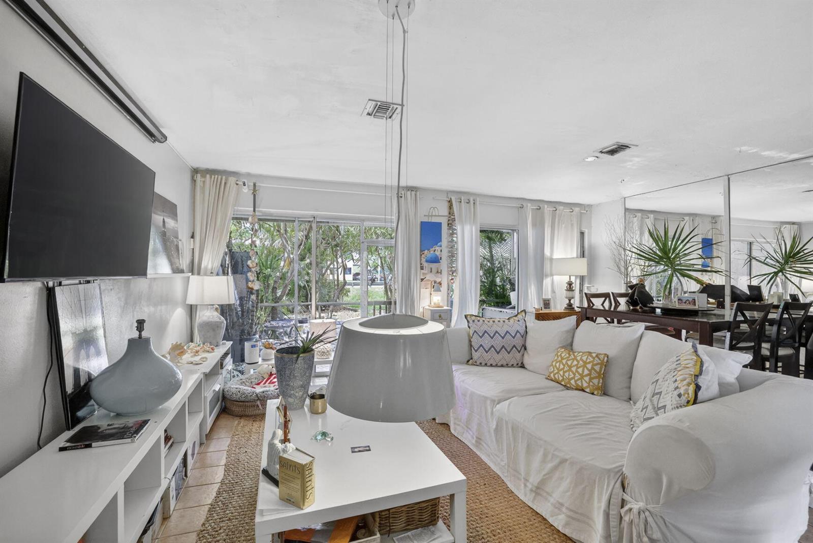 A bright living room features a white sofa, a coffee table, and a large television — 153 W Hemingway Circle W, Margate FL 33063, MARGATE, FL