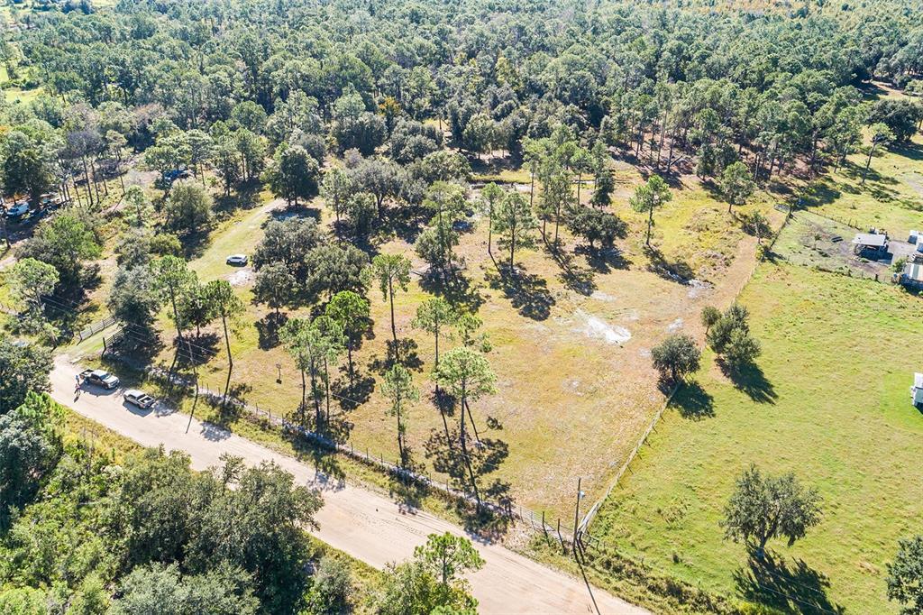 An aerial view shows a fenced, grassy lot with scattered trees along a dirt road — 1405 FAZZINI DRIVE, FROSTPROOF, FL