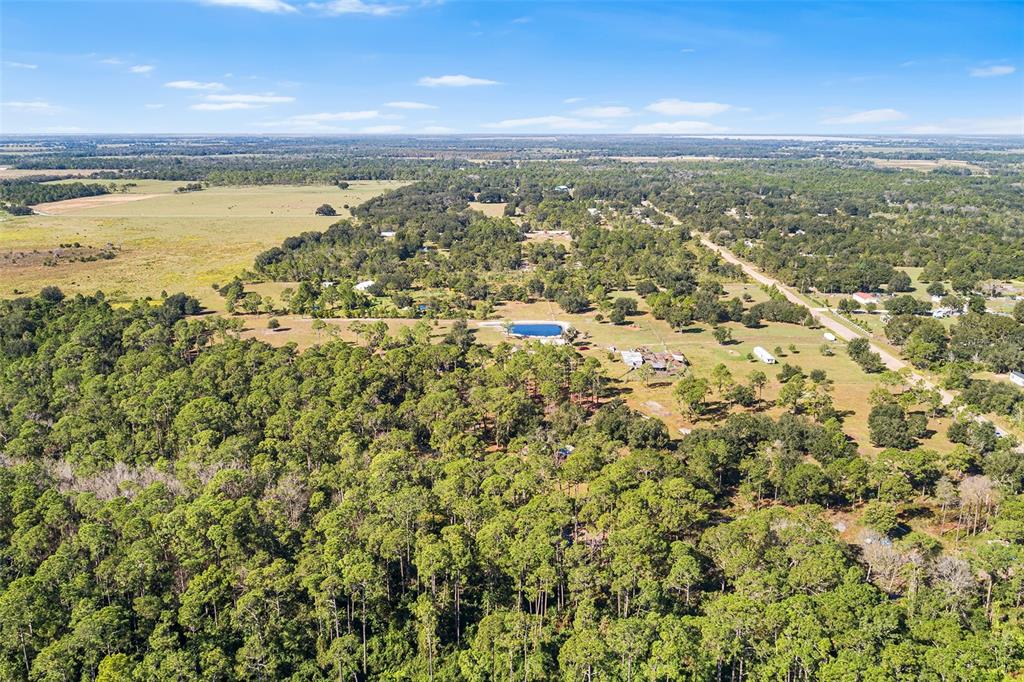 An aerial view shows a rural landscape with dense forest, open fields, and a small pond — 1405 FAZZINI DRIVE, FROSTPROOF, FL