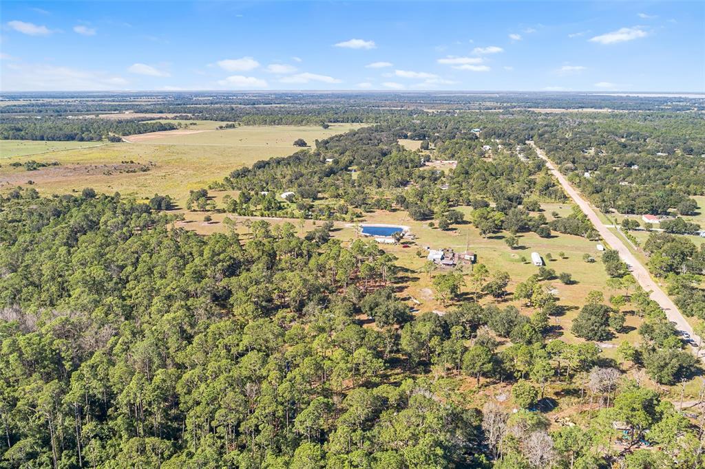 An aerial view shows a rural property with a pond, scattered trees, and a road — 1405 FAZZINI DRIVE, FROSTPROOF, FL