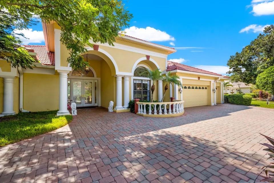 A yellow house with a red tile roof, arched entryway, and a brick paver driveway — 30324 LAURELWOOD LANE, WESLEY CHAPEL, FL