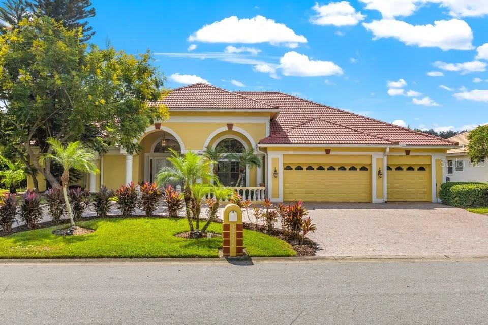 A yellow single-story house with a tile roof, three-car garage, and a landscaped front yard — 30324 LAURELWOOD LANE, WESLEY CHAPEL, FL