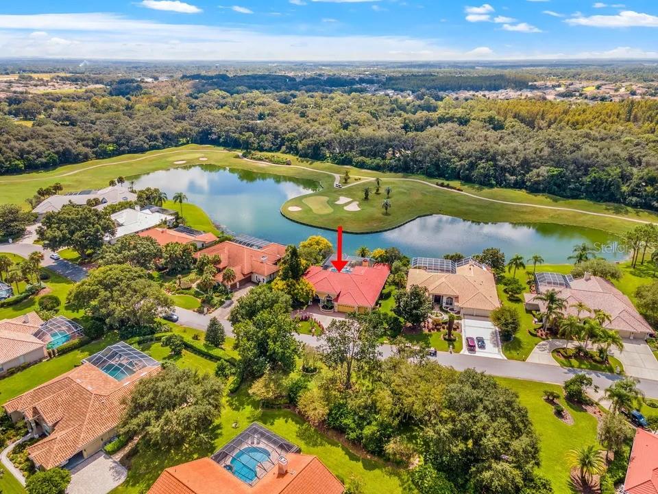 An aerial view shows a house with a red roof overlooking a lake and golf course — 30324 LAURELWOOD LANE, WESLEY CHAPEL, FL