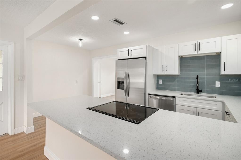 A kitchen features white cabinets, stainless steel appliances, a blue tile backsplash, and quartz countertops — 3733 SURREY DRIVE, ORLANDO, FL