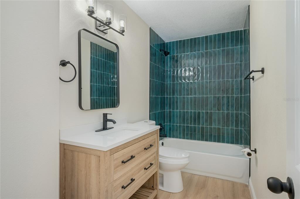 A bathroom features a wood vanity, white countertop, and a shower with teal vertical tiles — 3733 SURREY DRIVE, ORLANDO, FL