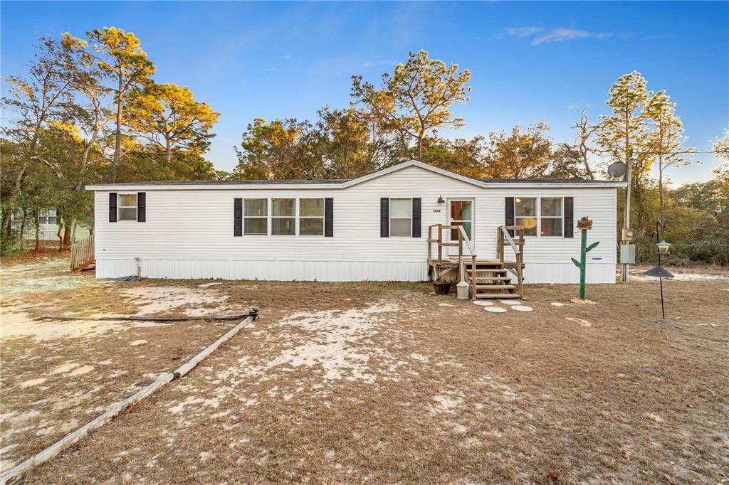 A white single-wide mobile home with a wooden front porch sits on a sandy lot — 6072 W PATRIOT STREET, HOMOSASSA, FL