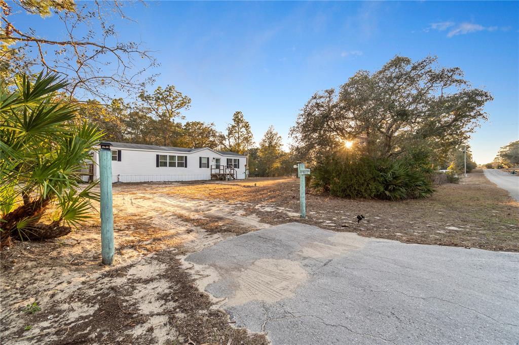 A white mobile home sits on a sandy lot with a paved driveway in the foreground — 6072 W PATRIOT STREET, HOMOSASSA, FL