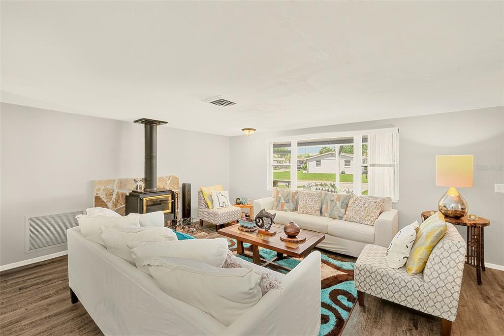 A living room features a wood-burning stove, white sofas, patterned armchairs, and wood-look flooring — 5126 ROSEWOOD DRIVE, NEW PORT RICHEY, FL